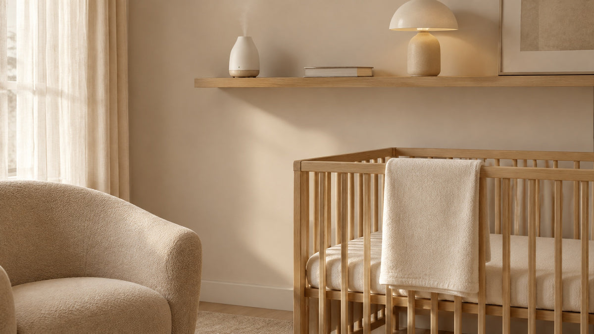 A calm nursery with an empty oak crib, a folded blanket and a cream armchair in soft daylight